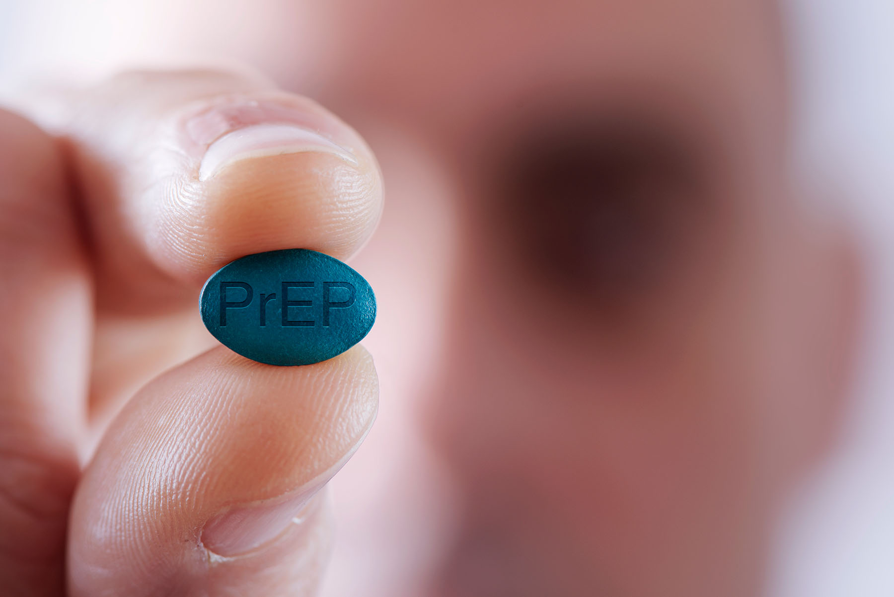 Close up of light skiined man holding a Prep pill to the camera.