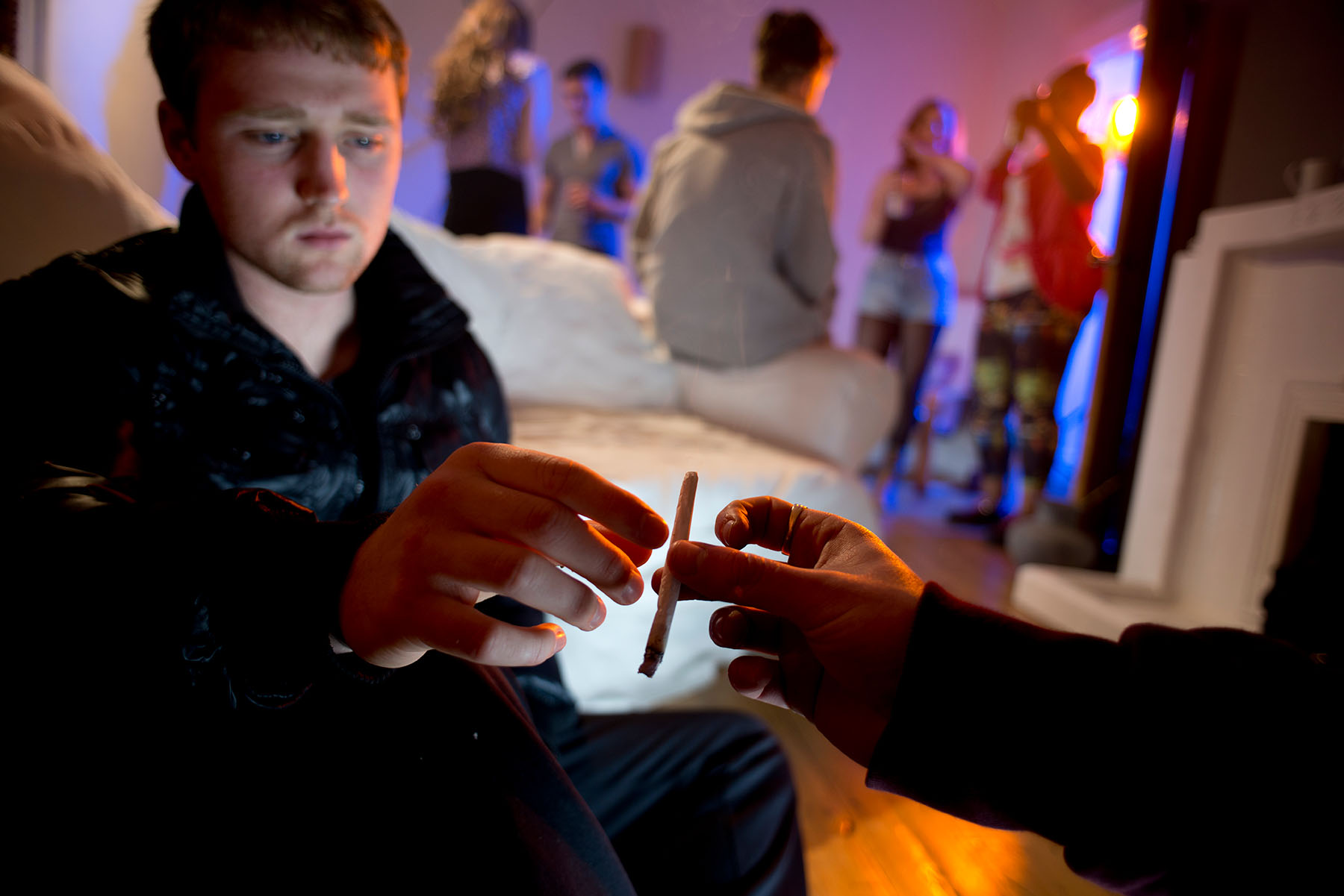 Teen boys in foreground at at party sharing a marijuana cigarette.