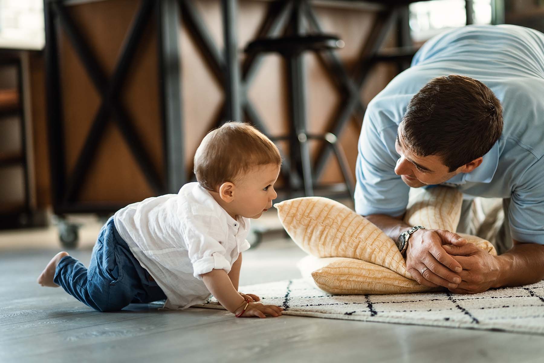 Well dressed toddler crawls to Dad who is crouched on floor at baby's level.