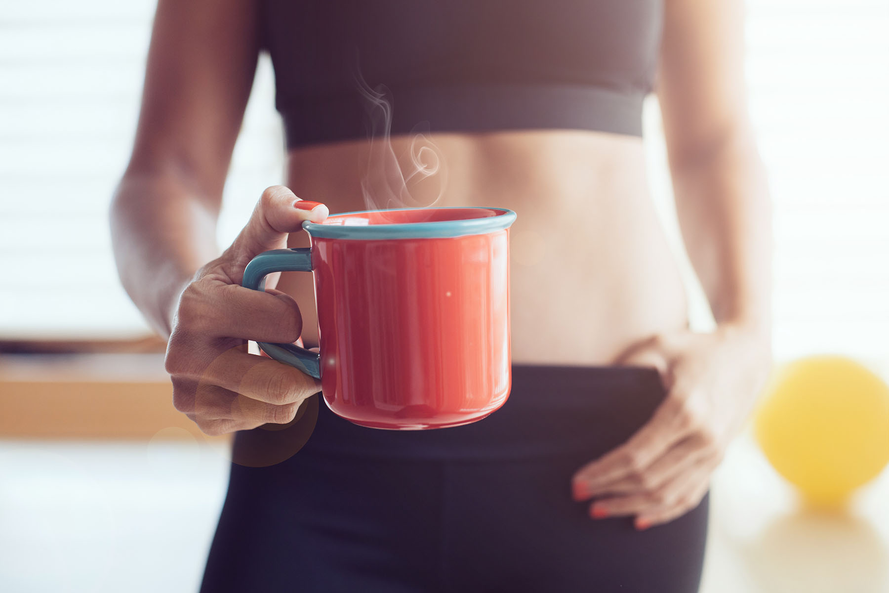 Female athlete holds a steaming cup of coffee in a red mug.