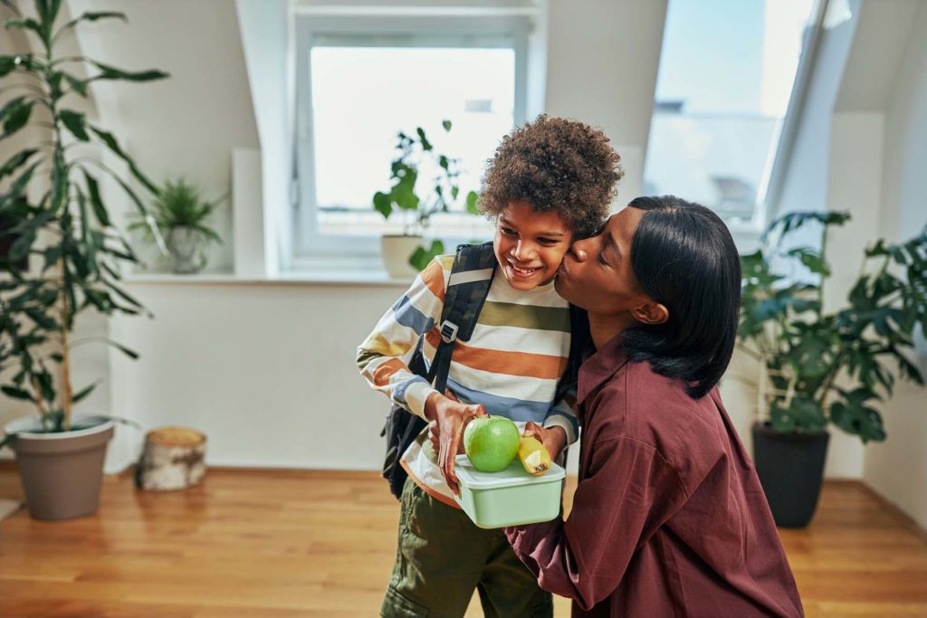 Black child gets a kiss and a healthy packed lunch from Mom.