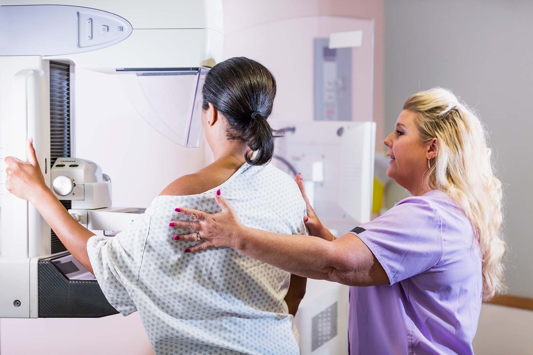 Black woman leans into mammogram tool while nurse assists.