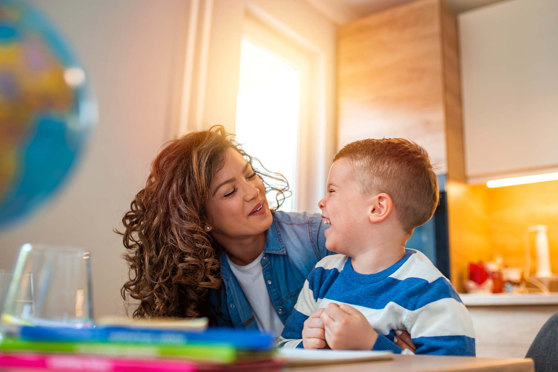 Pretty Hispanic mom and son are smiling while working on homework.
