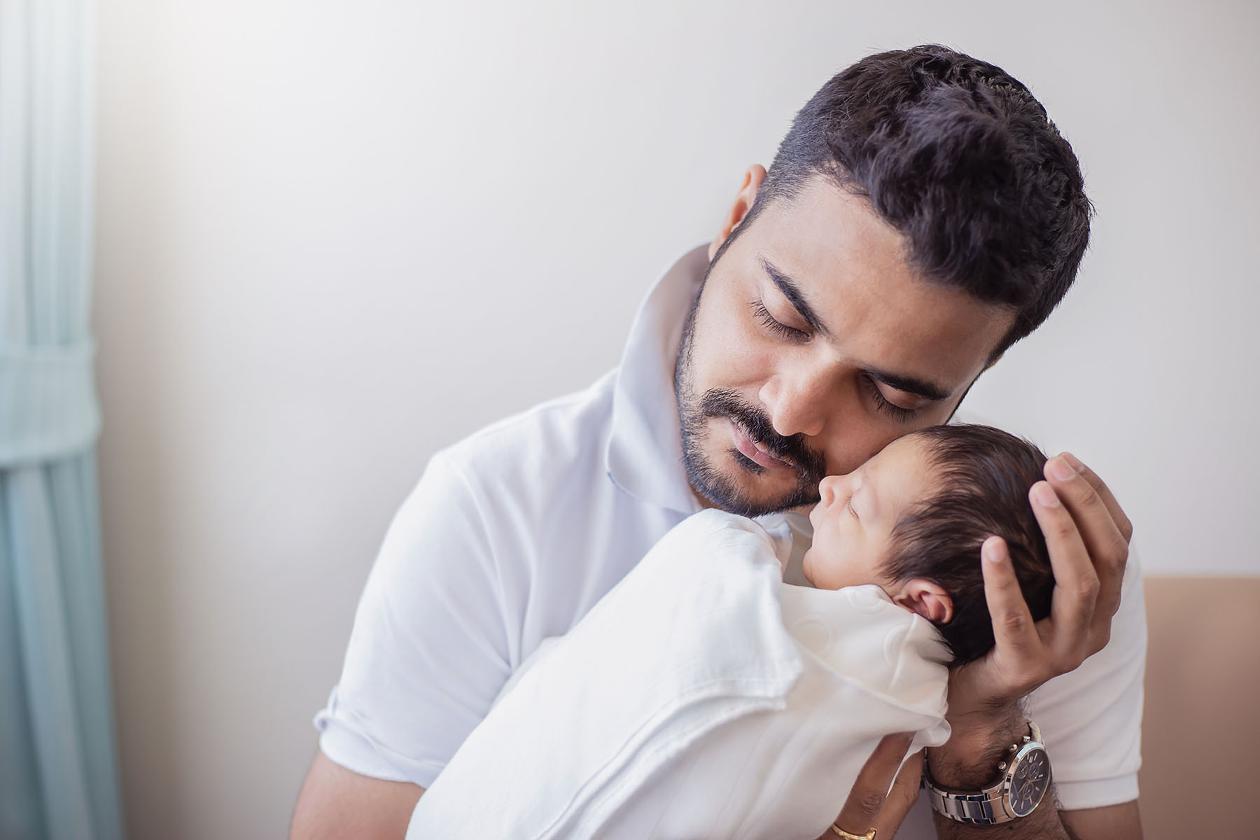 Hispanic man embraces new baby in a swaddle.