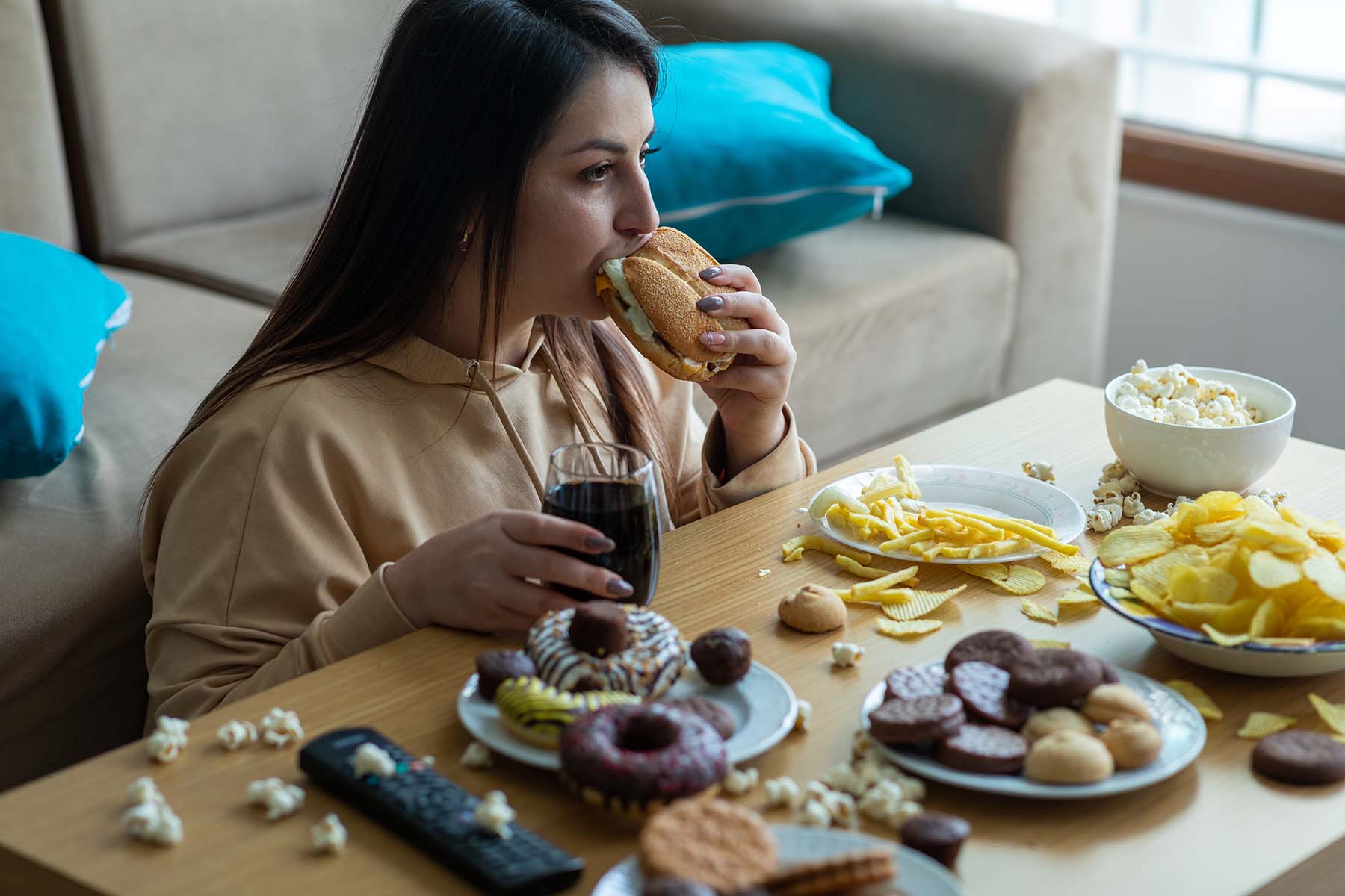 Woman sits in front of a table full of junk food, obviously over eating.