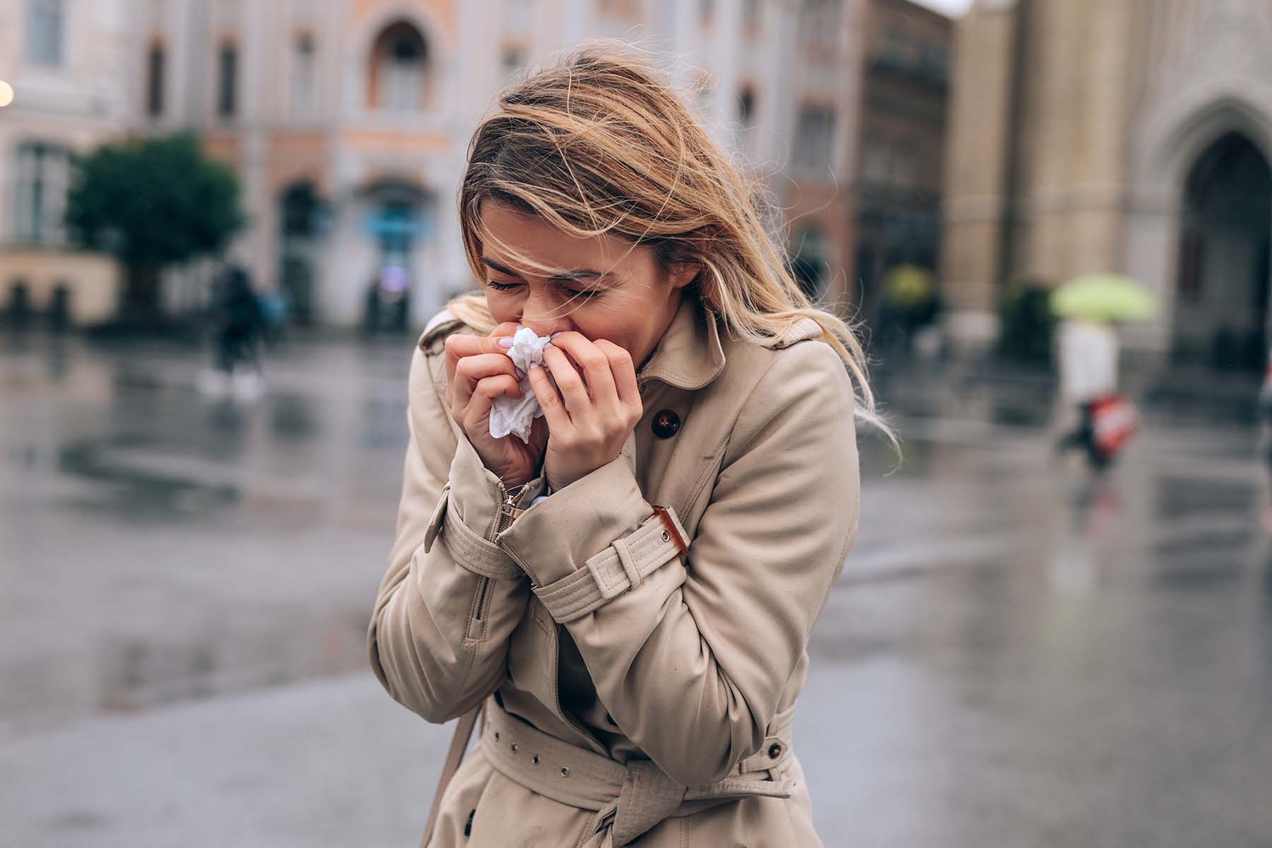 Lady walking down street in chilly weather blows her nose.