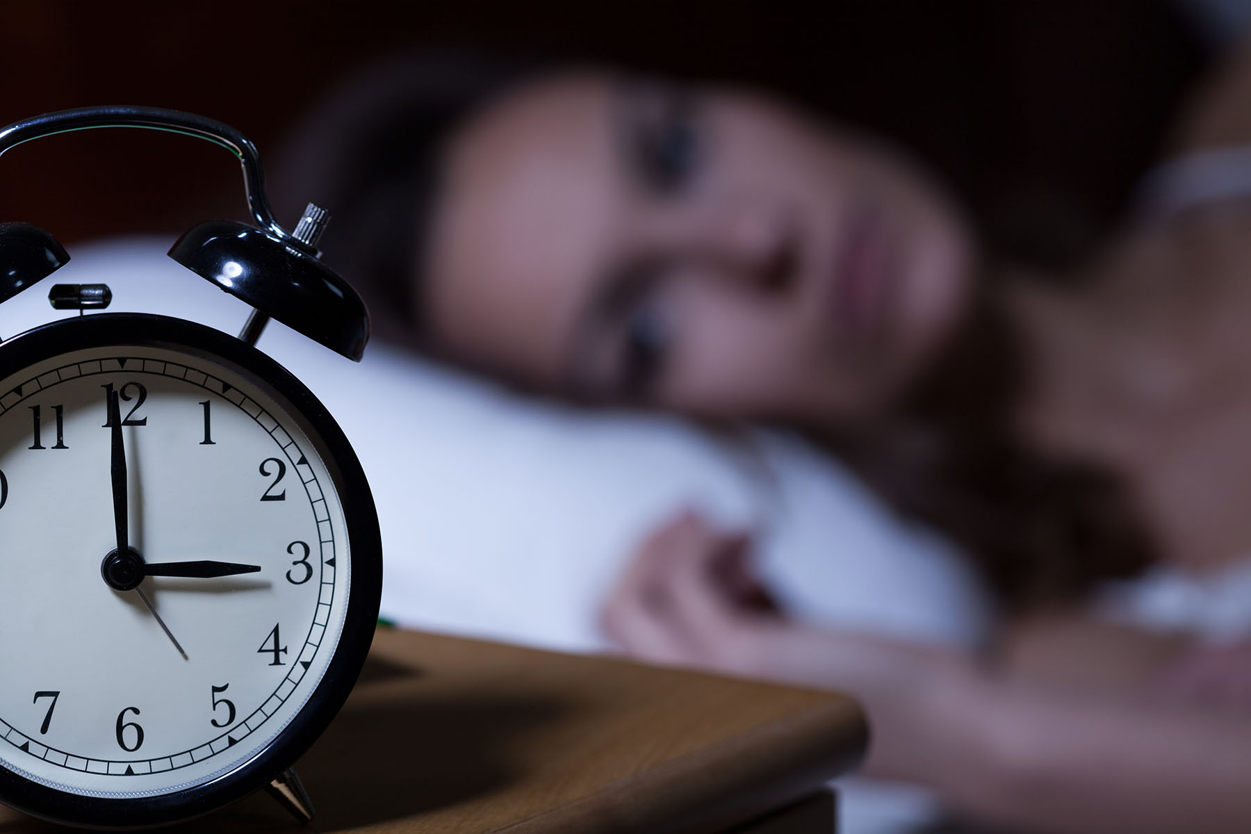 Bedside clock reads 3am as woman lies awake in background.