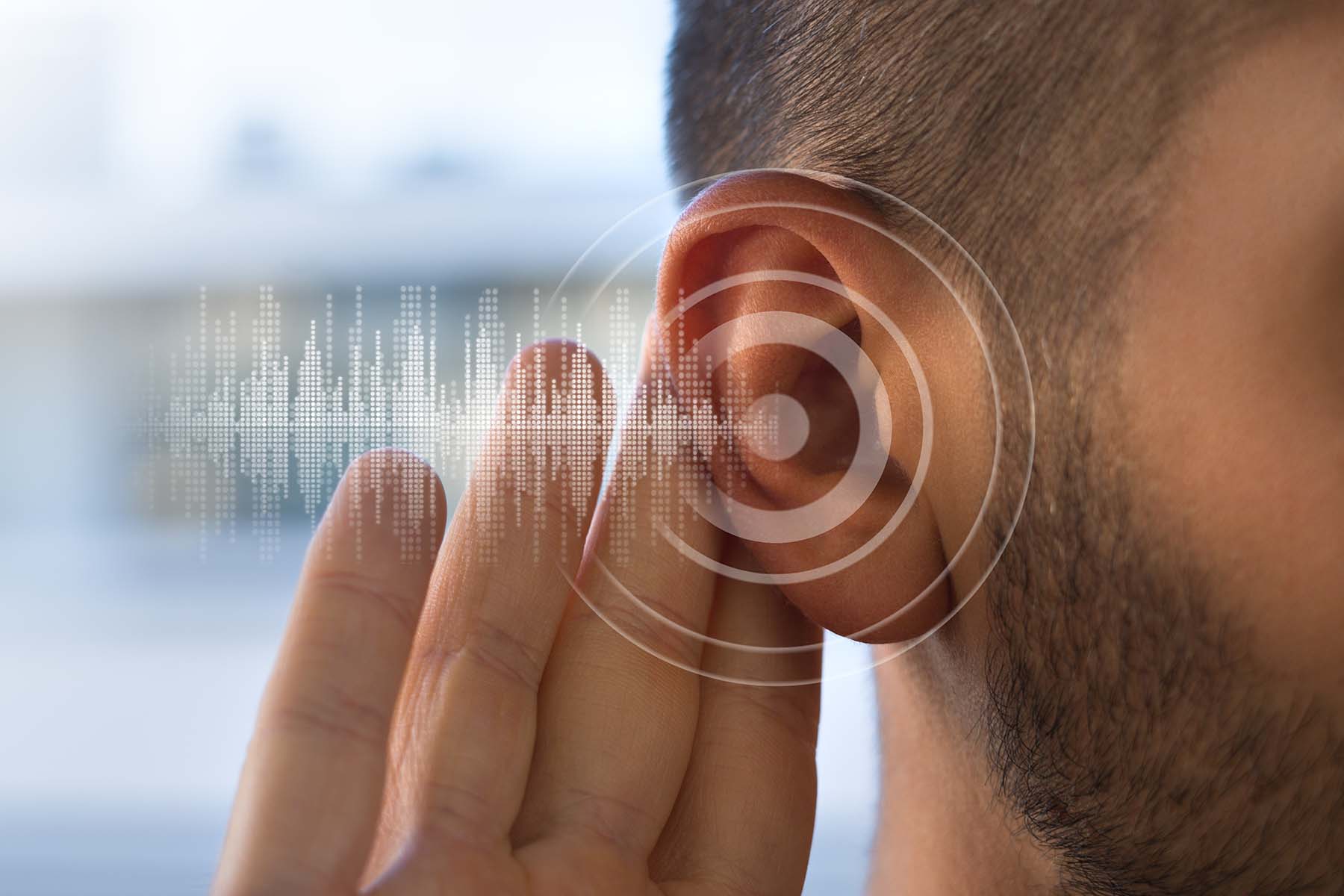 Close up of a young man holding his hand to his hear to hear better. Graphic of sound waves overlaid on image.