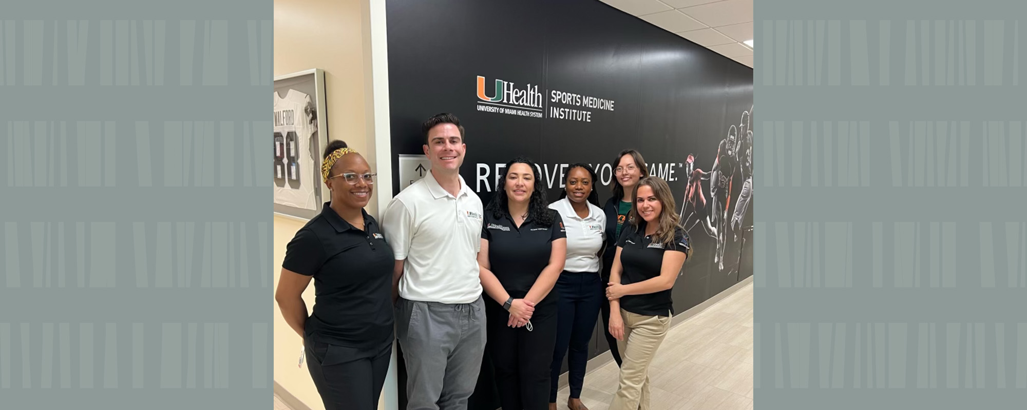 The team of athletic trainers at UM's Sports Medicine Institute gathered in front of hallways sign.