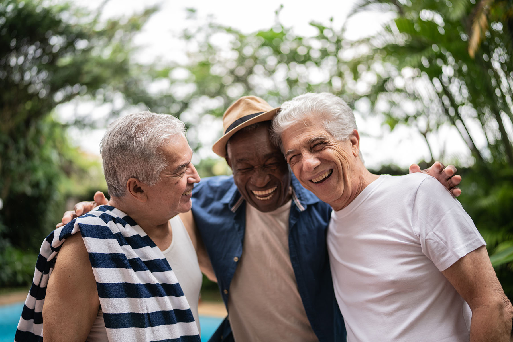 Three senior men embracing, enjoying a pool party.