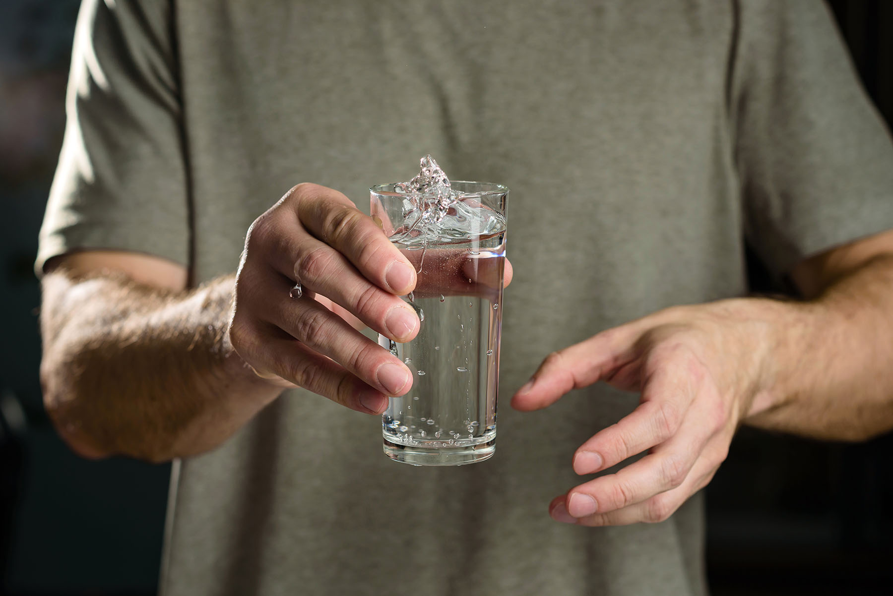 Close up of a man's hands. He's holding a glass of water which shakes from his tremors.