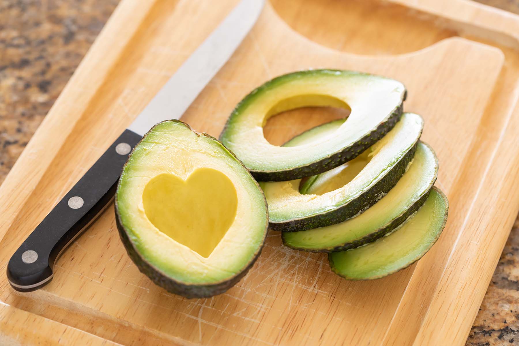Avocado cut up on carving board. Half has a heart shape carved out to show avocado is good for heart health.