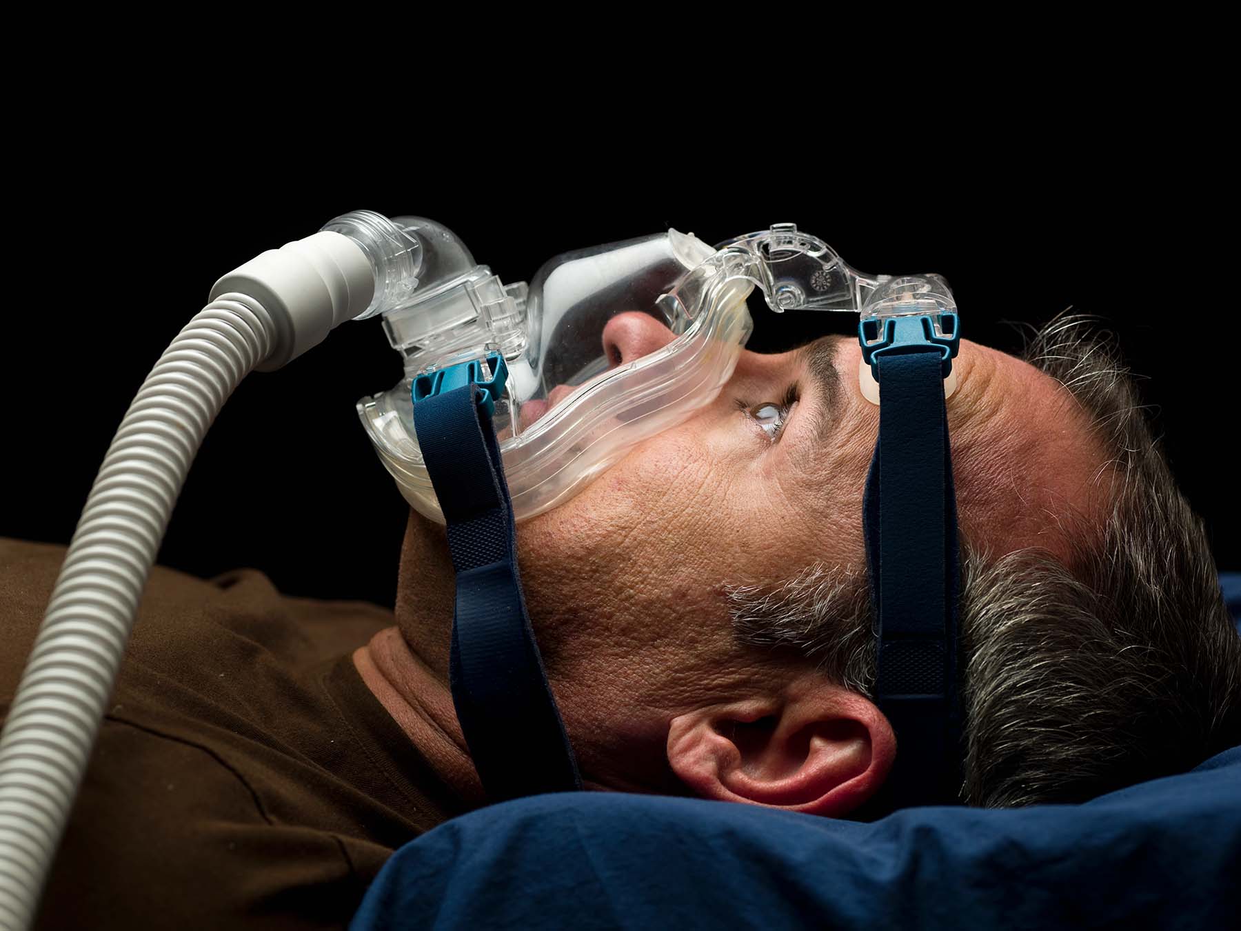 Older man lying own awake, wearing CPAP mask