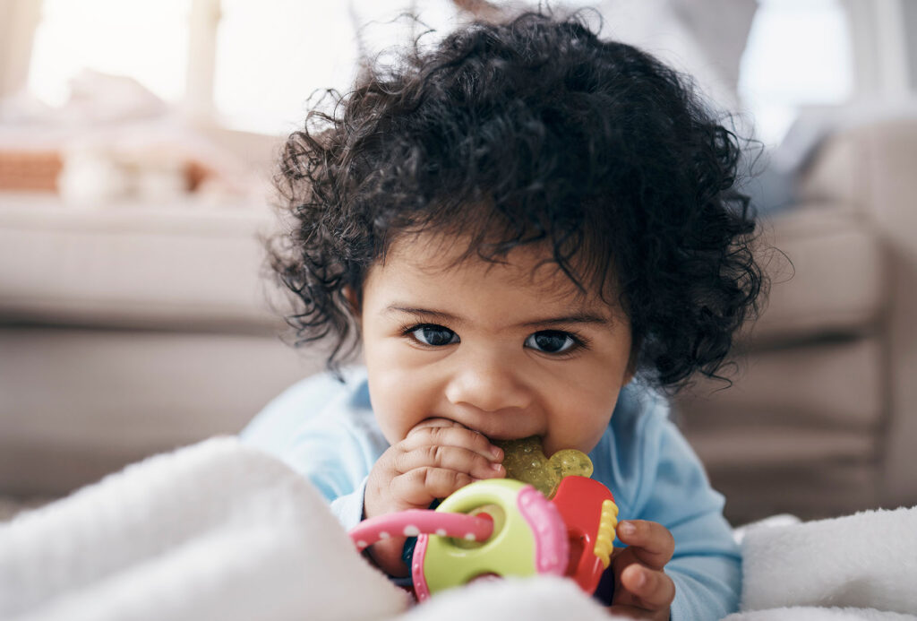 Baby lies on floor chewing on teething toy