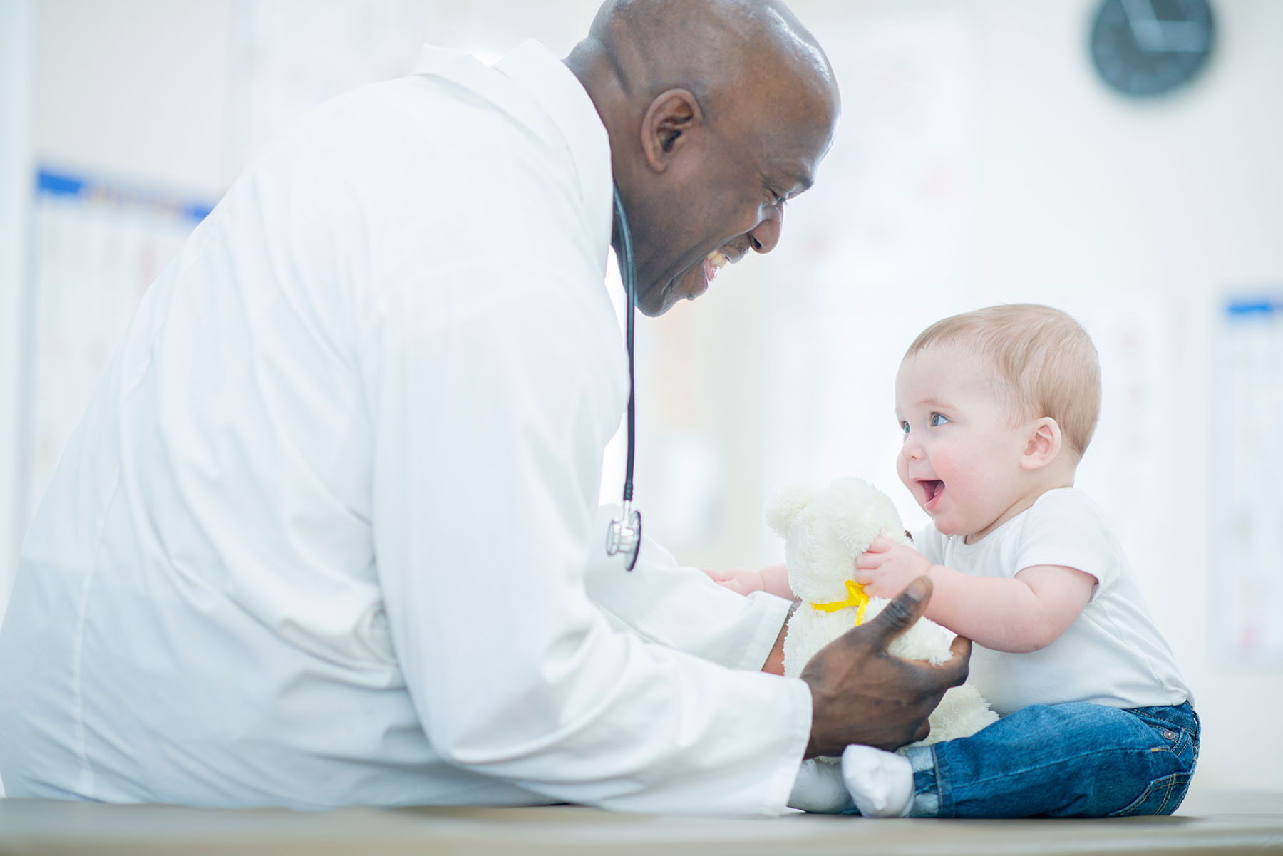 Black male pediatrician gives caucasian baby a checkup.