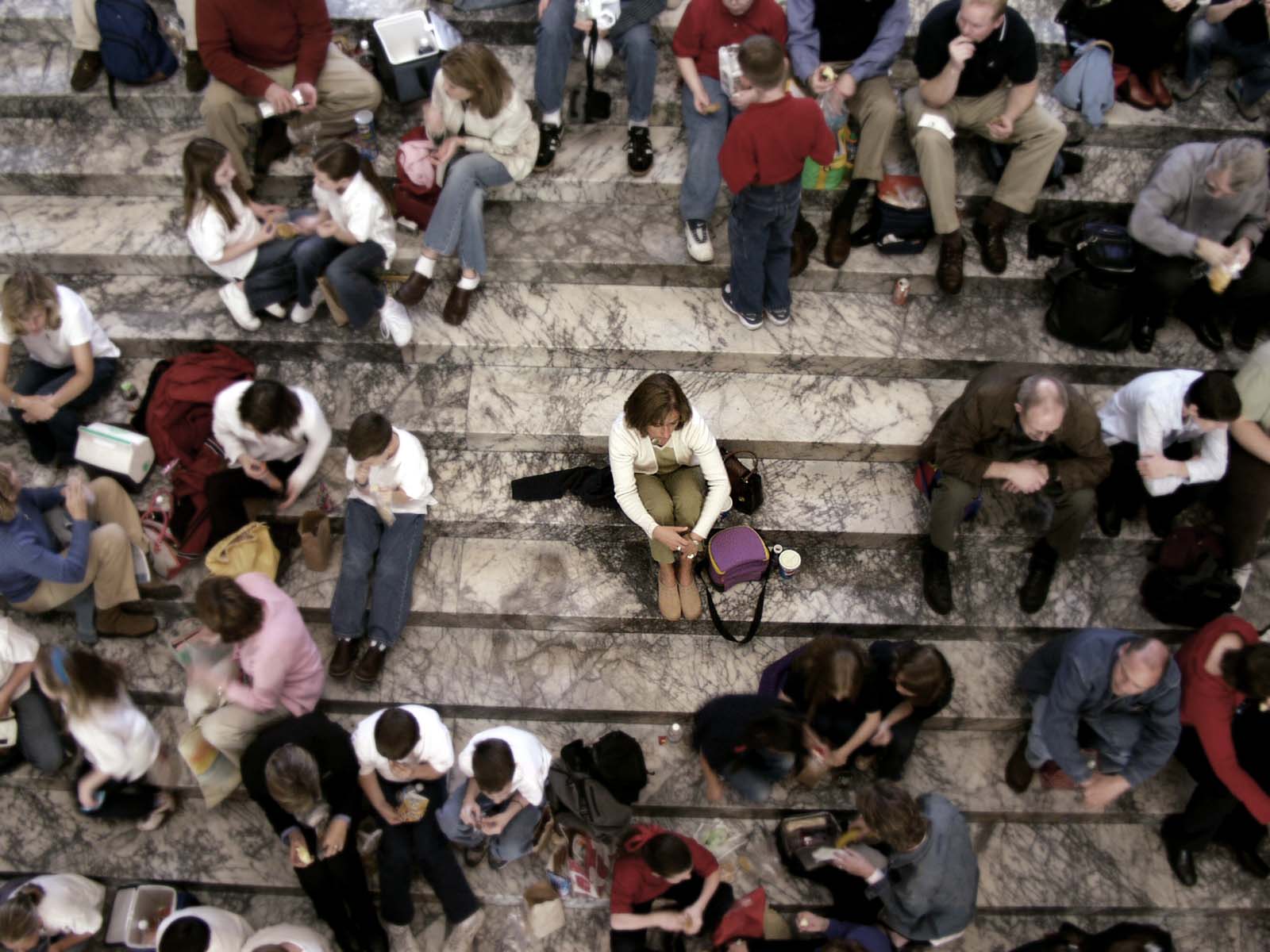 A lot of people sitting on steps. A woman in the middle of crowd appears alone.