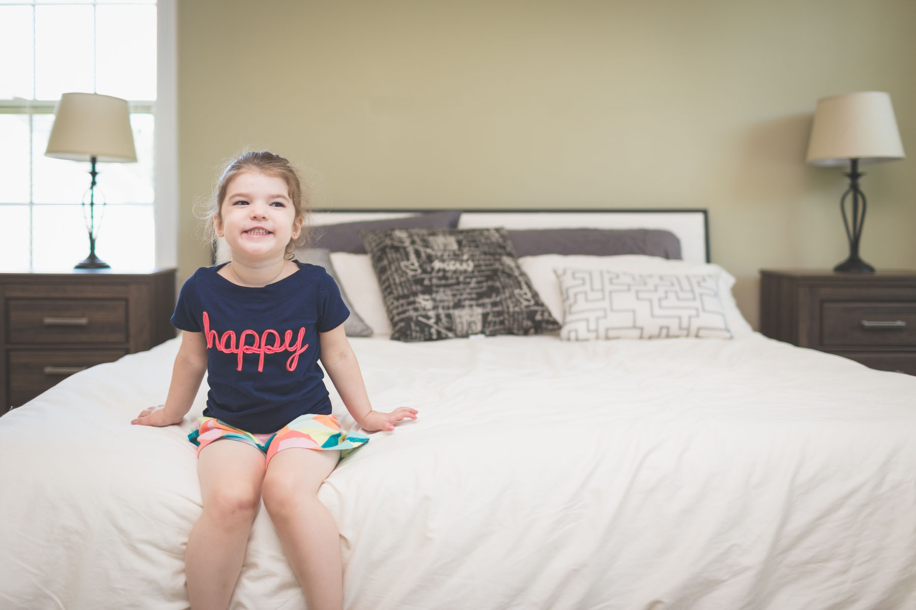 Happy young girls sits calmly smiling at the end of beautiful, modern bed.