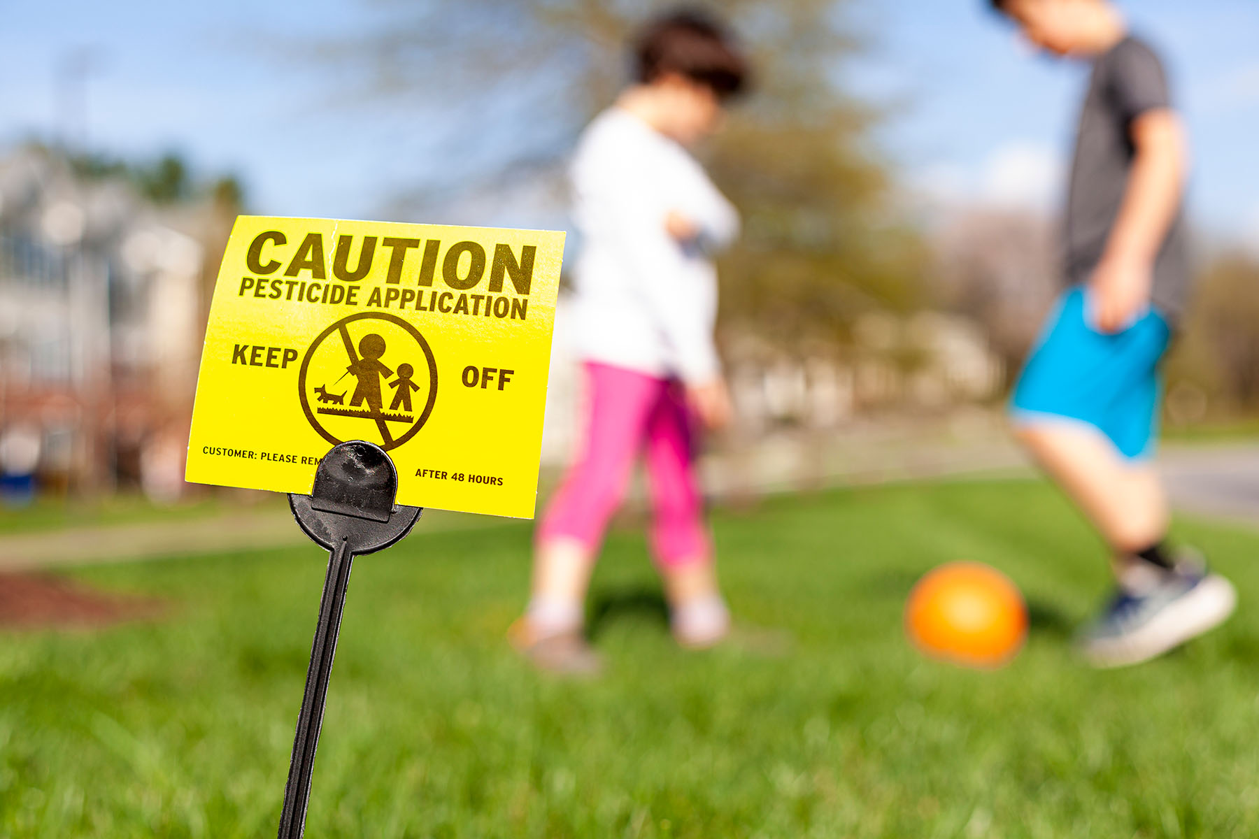 Kids playing behind a sign warning about pesticides in lawn.
