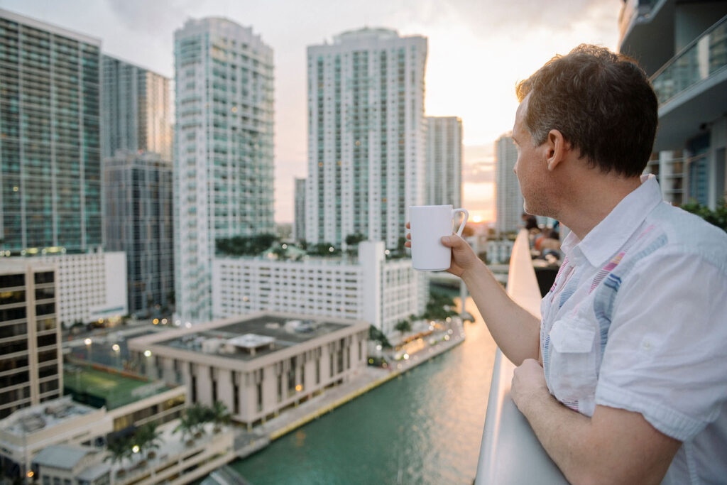 Man holds coffee mug while looking out over Brickell in Miami.