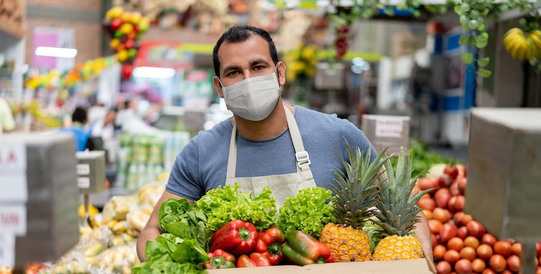 Latin American man carries box of vegetables while wearing a COVID mask.