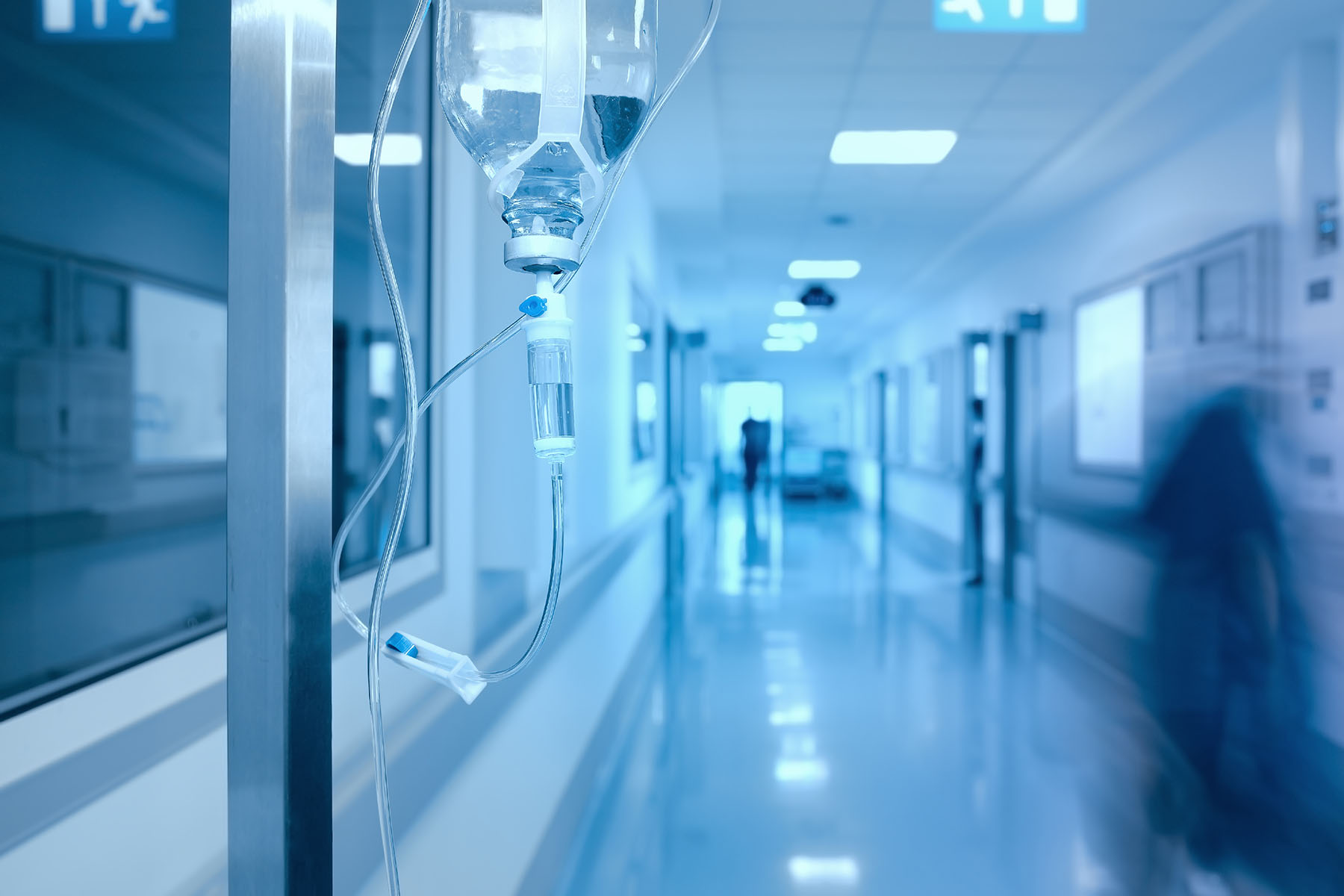 A blue hue shows a hospital hallway with an IV drip in foreground.