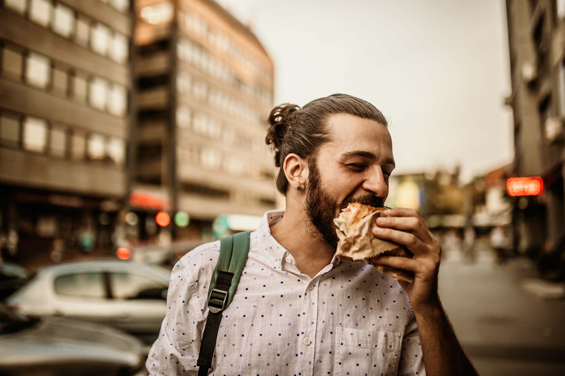 Man enjoys vendor yummy, mouth-watering sandwich while walking down street.