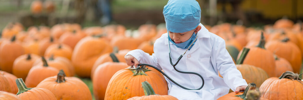 child in doctors costume on Halloween checking a pumpkin's health with a stethoscope