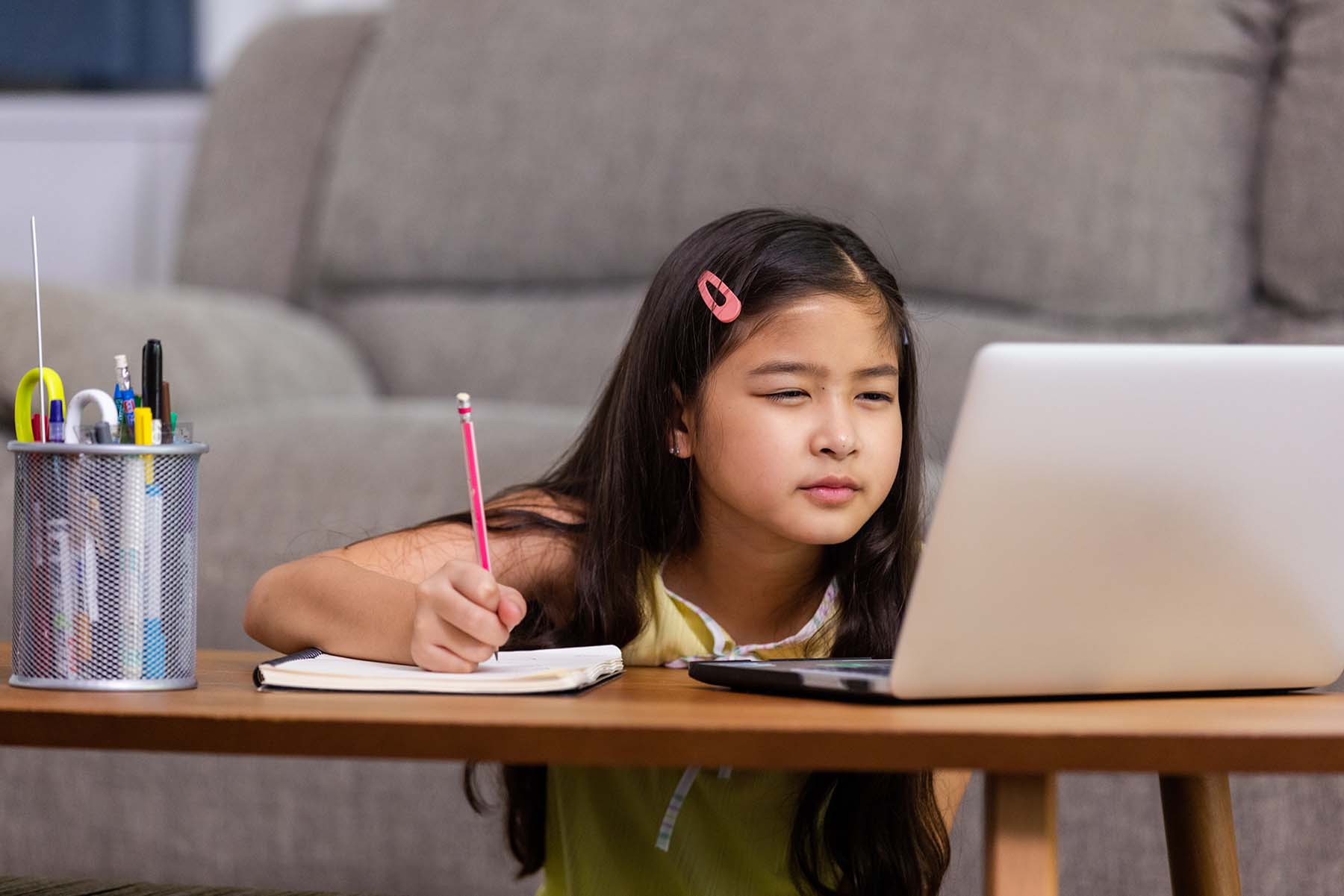 Little girl squints at computer screen while doing her homework.