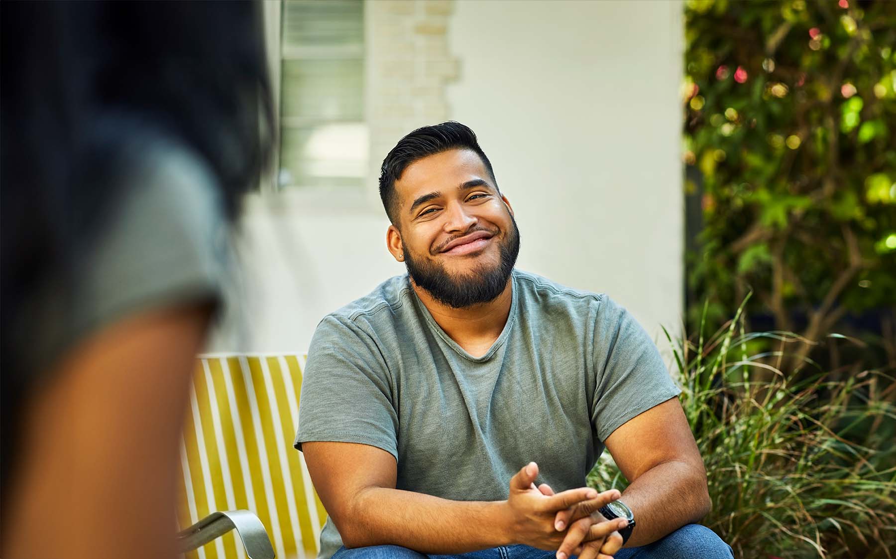 Young Hispanic man sitting outside smiles sheepishly as he quits vaping.