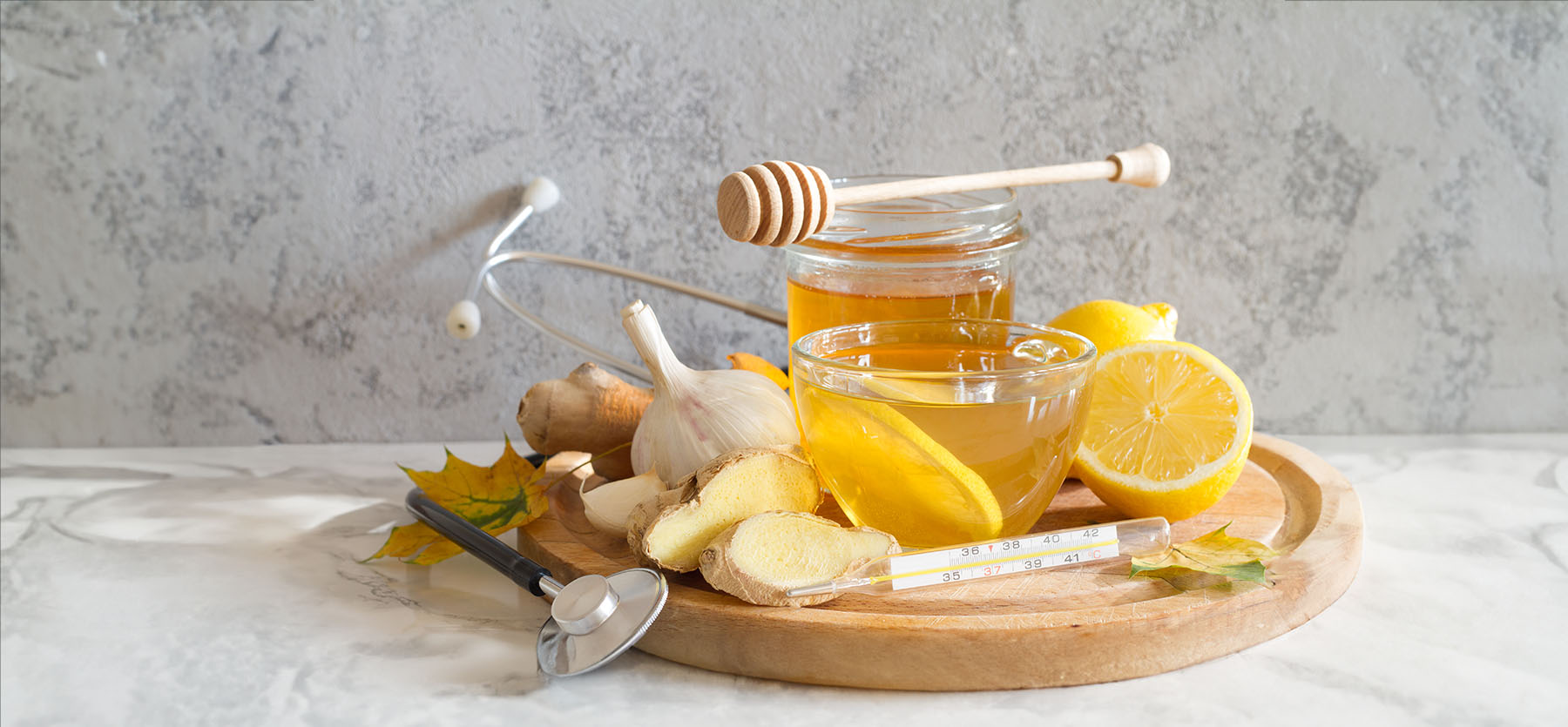 Picture of honey, lemon, onion and other natural remedies wrapped in a stethoscope. Set against a grey stone backdrop.