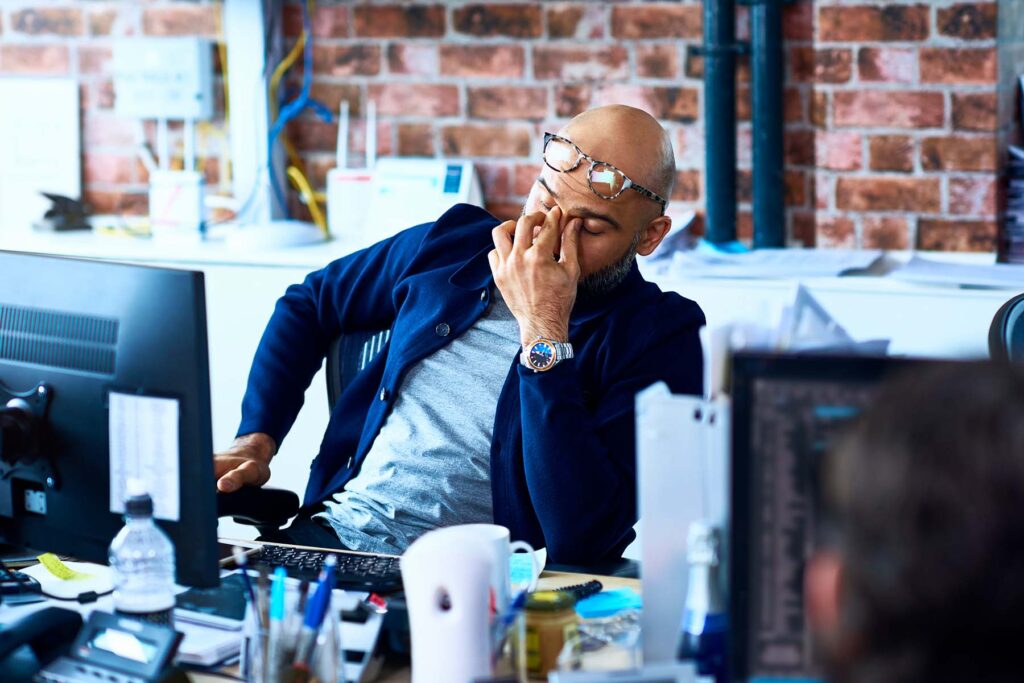 Bald man moves his glasses and rubs his eyes to fight off feeling tired while working.