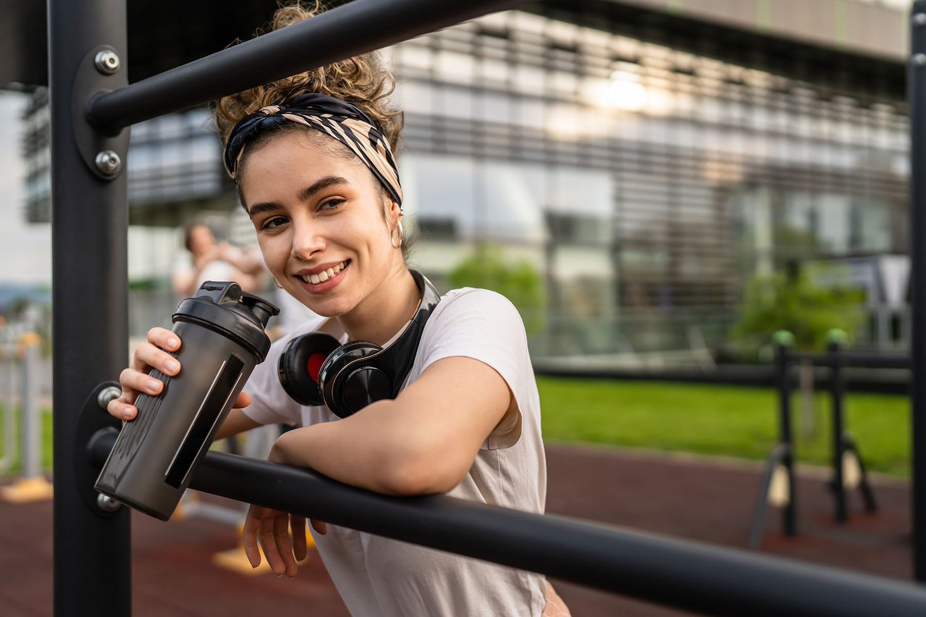 Young woman rests on a railing after a workout and drinks protein shake.