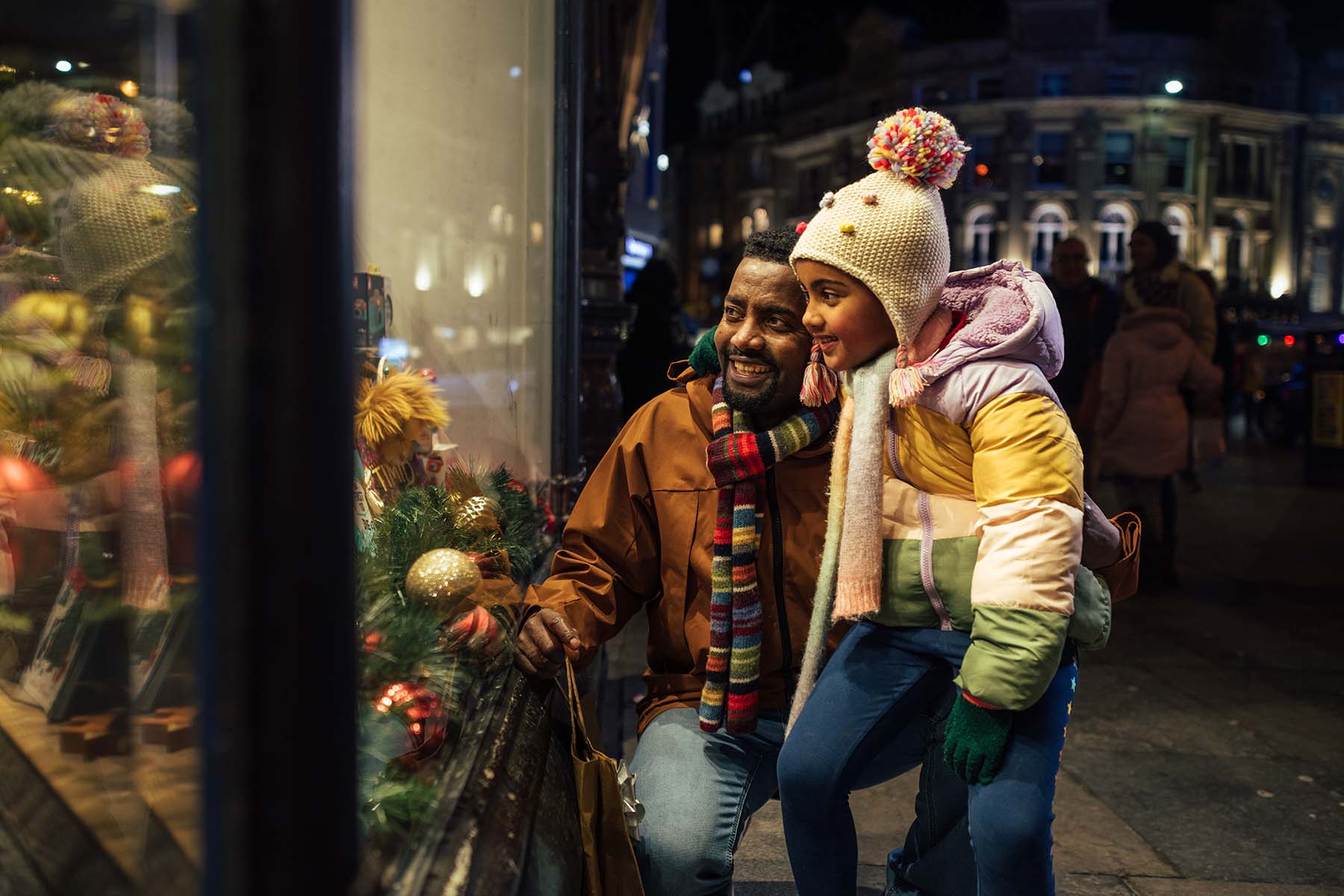 Dad and daughter smiling at a pretty holiday window display in a city with cold weather.