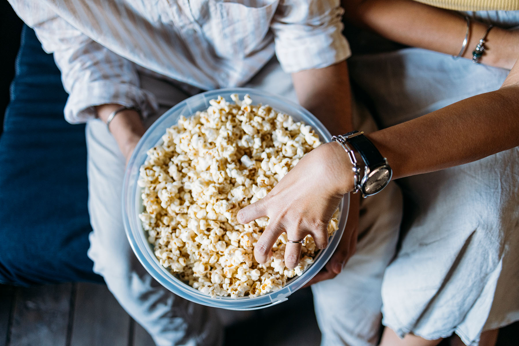 Photo of a big popcorn bowl with hands reaching in.