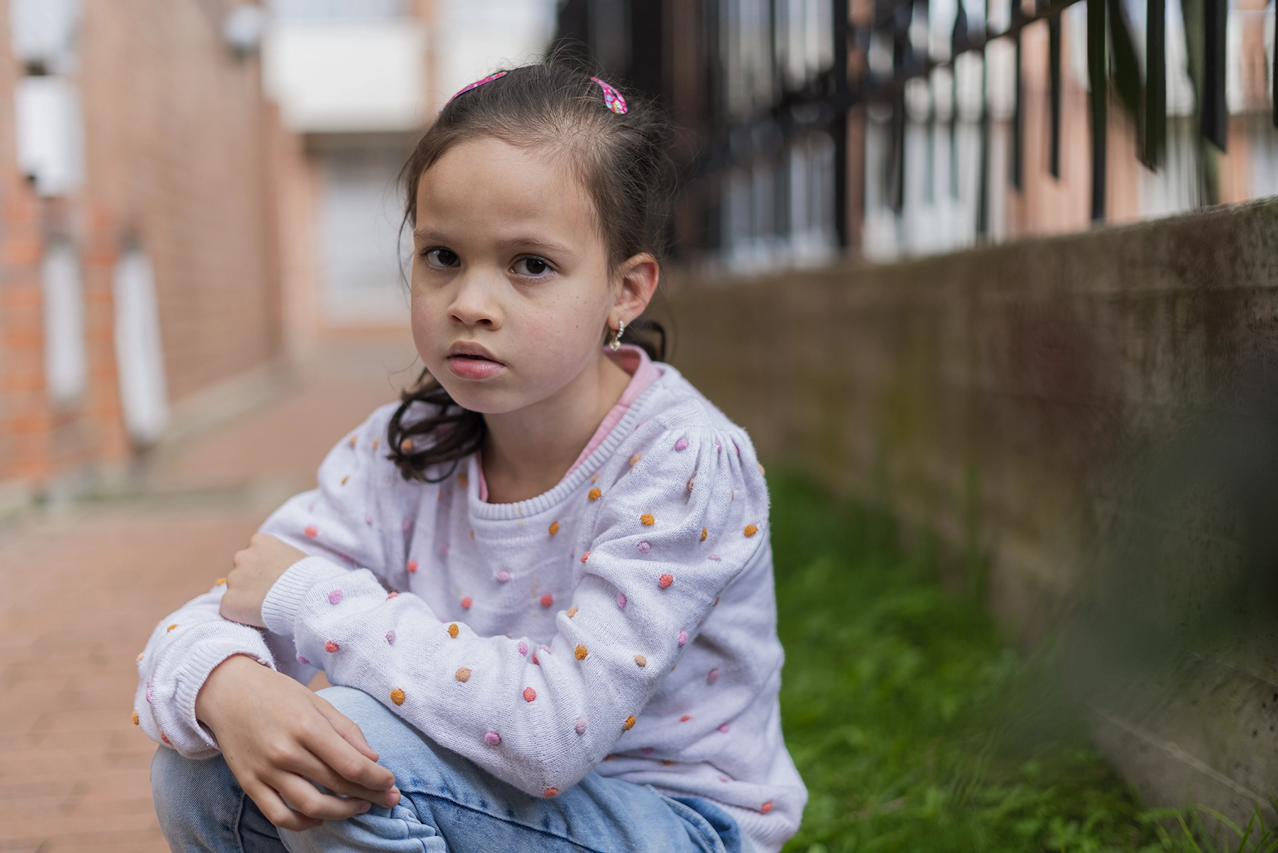 Young Hispanic girl is sitting outside a school by herself and appears to be sad.