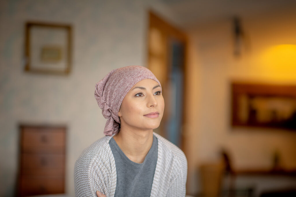 Young ethnic woman with a headscarf after cancer treatment looks at peace in her living room.