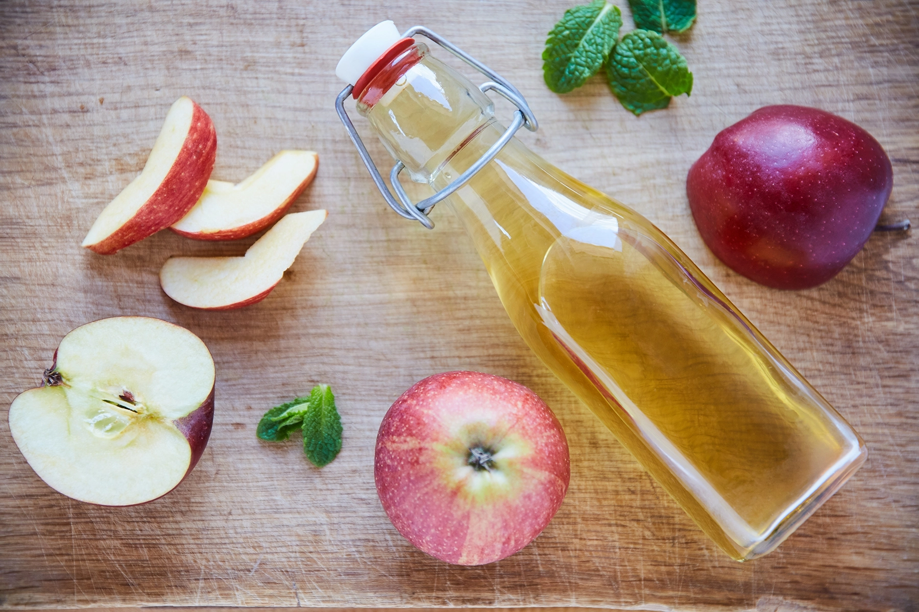 An overhead shot of a bottle of apple cider vinegar on a wooden table, surrounded by apples.
