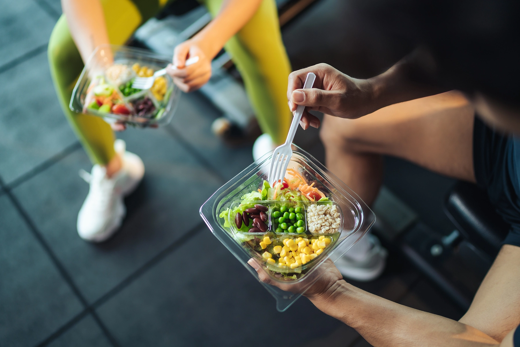 Overhead shot of two people at the gym eating protein-filled salad.