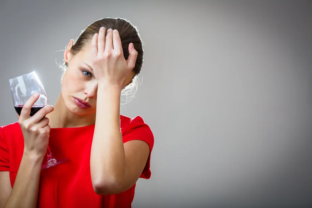 Woman in a red dress has a headache while drinking red wine.