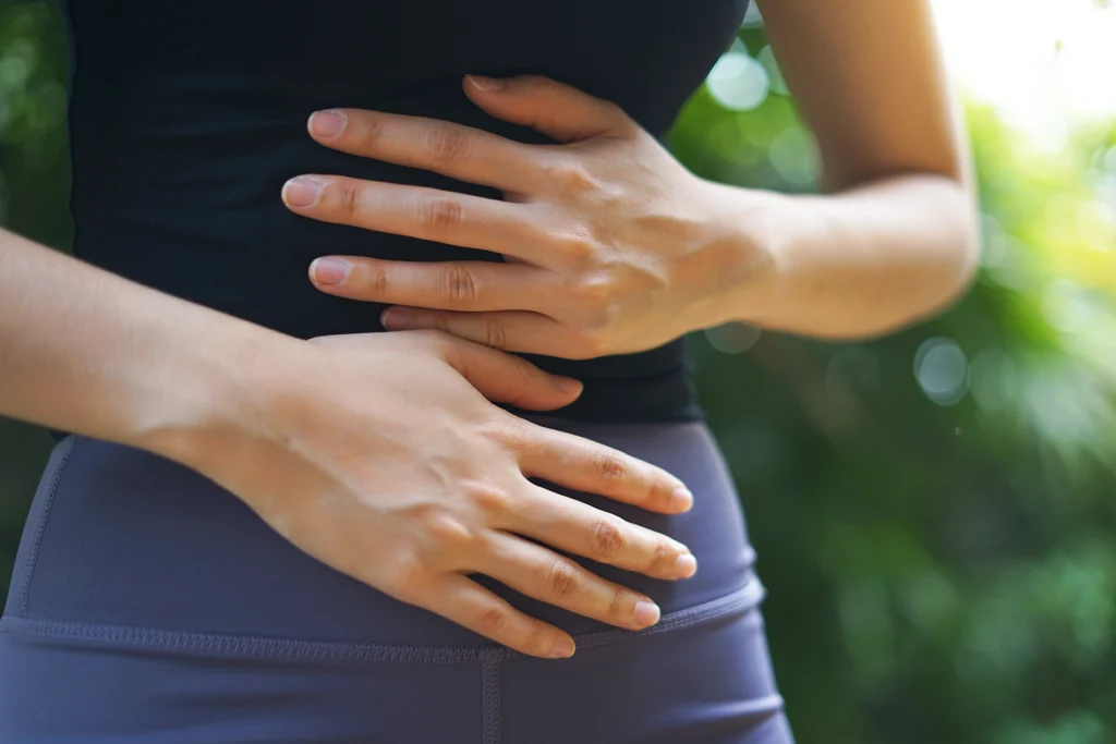 Close up of woman clutching her stomach in due to IBD or stomach pain.