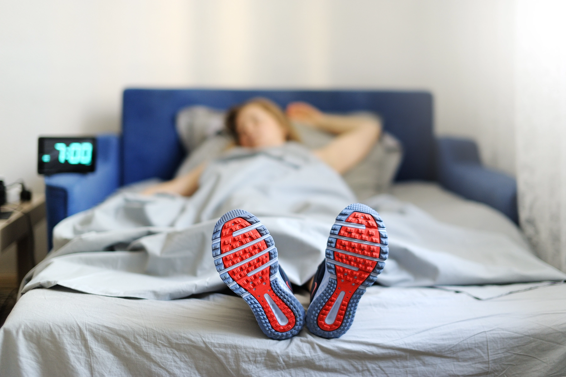 Woman in running shoes lies in bed prepping herself to get up. Clock shows 7am.