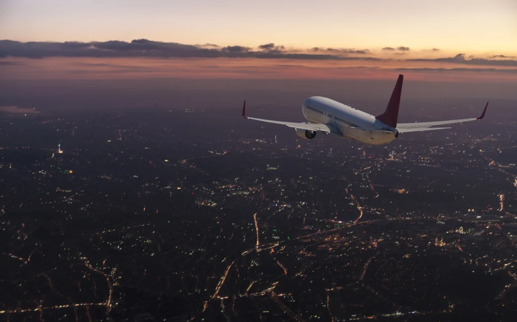 Photo of a large commercial airliner flying over a city at dusk.