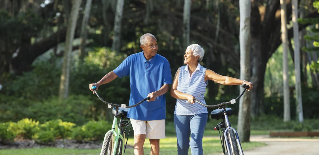 Black senior couple walking beside their bikes, having a nice conversation.