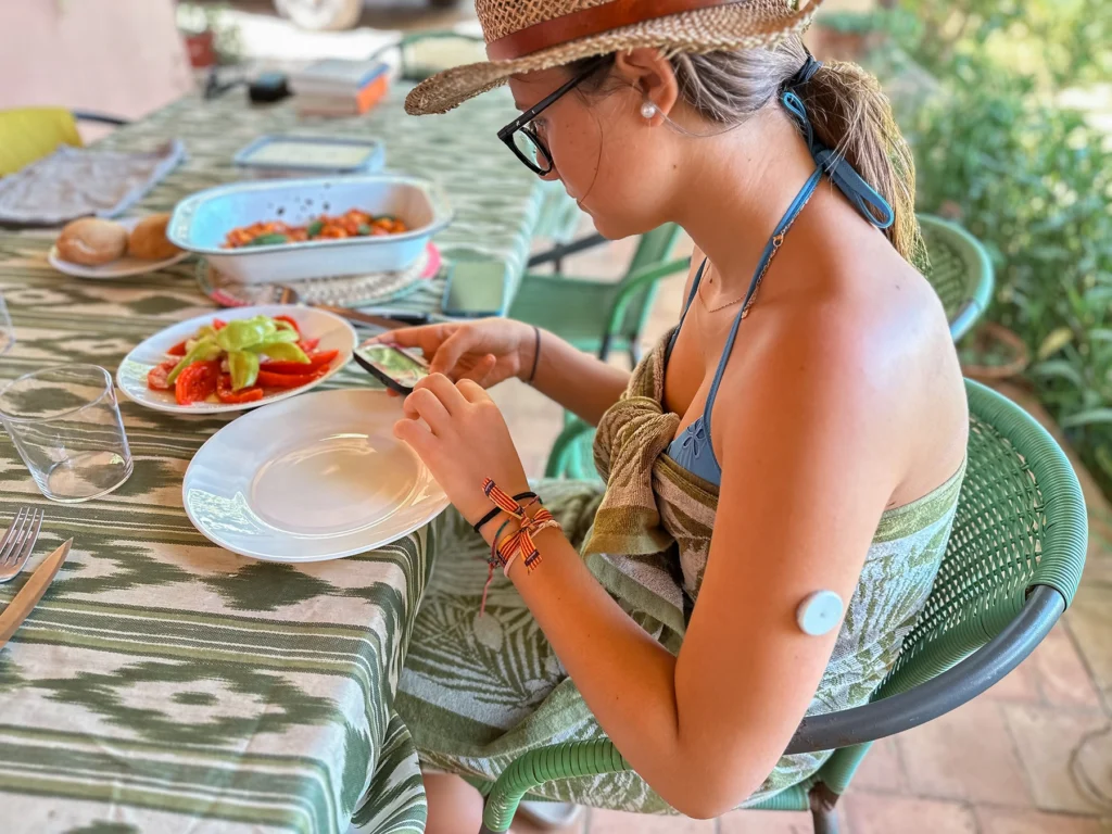 Young woman with a CGM device sits down outside to enjoy a healthy meal.