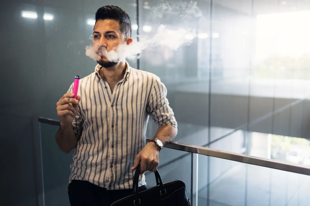A young hispanic man using a e-cigarette indoors, a growing vaping health concern