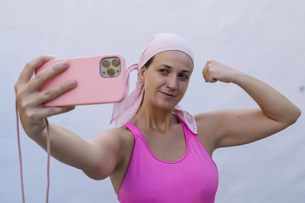 Woman with cancer flexes while taking a selfie.