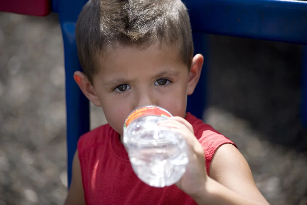Cute Hispanic boy drinks water in the shade to stay cool in the heat.