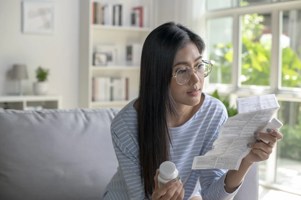 Young Asian woman carefully reads her medication instructions to see if there are any side effects.