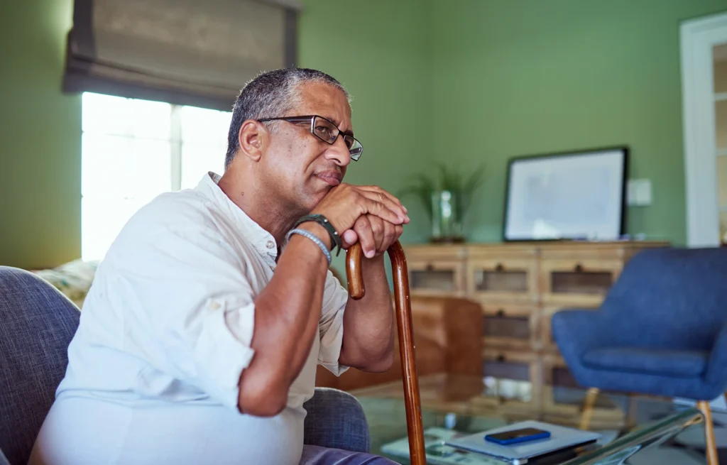 Older Hispanic man leans on his cane as he prepares to stand up slowly.