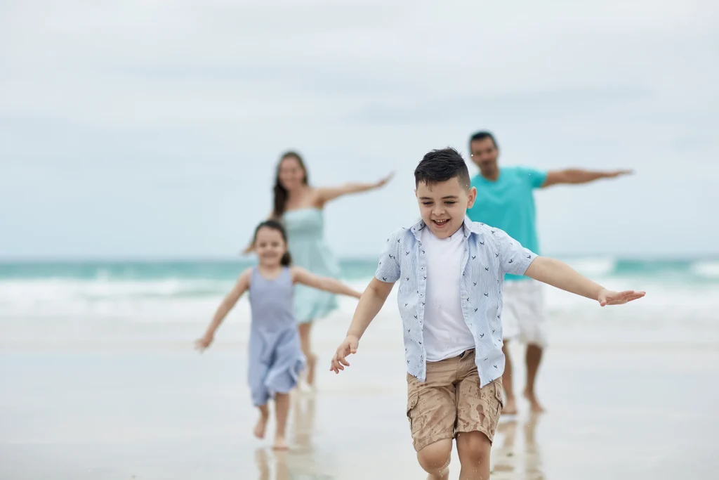 Happy young boy runs on beach with his family.